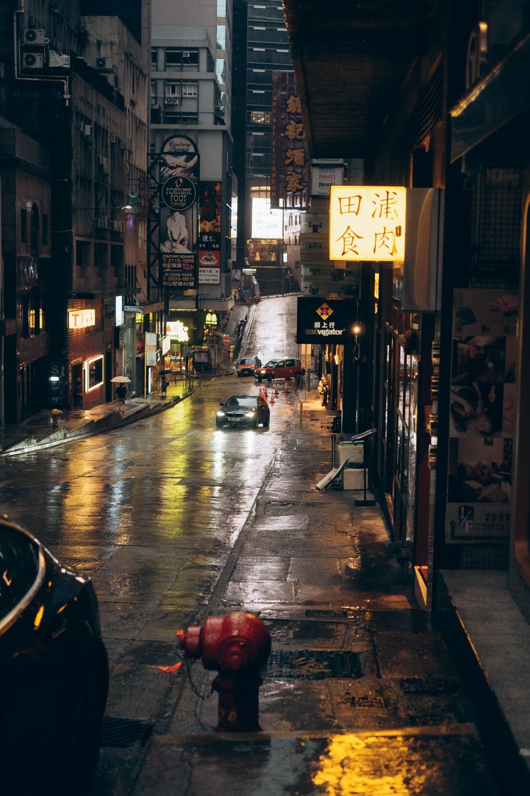 Rua estreita de Hong Kong à noite, molhada de chuva, letreiros acesos.